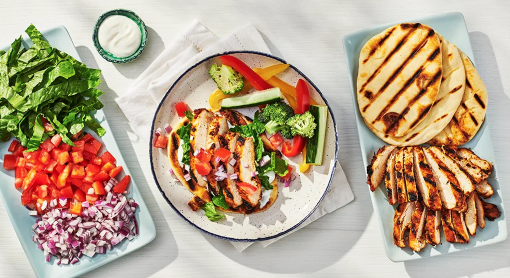 A colourful spread of Epicure meal including grilled chicken wraps, bright veggies for stir-fry, and flavourful sauce—this is a delicious dish we can get excited about when Epicure returns in Summer 2025.